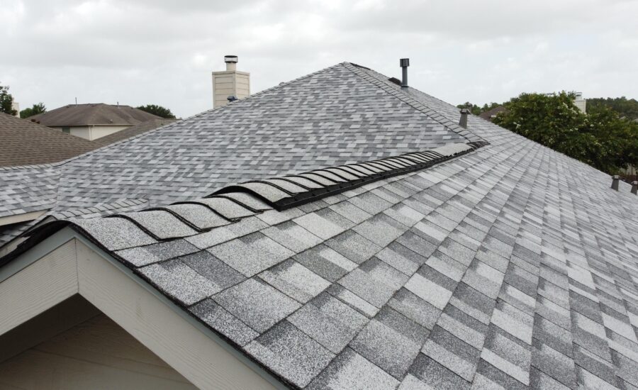 Aerial view of grey shingled rooftops with chimneys and vent pipes under a cloudy sky.